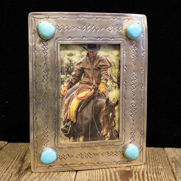 Custom Cowboy Shop. A silver picture frame with turquoise stones, containing a vertical photo of a person on horseback. The frame has a hand-stamped texture and decorative elements around the photo.