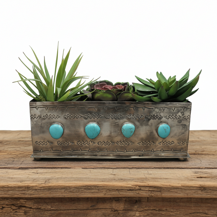 A silver planter box with turquoise stones, containing various plants.